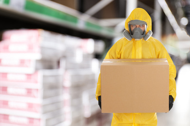 Image of Man wearing chemical protective suit with cardboard box in store. Wholesale market