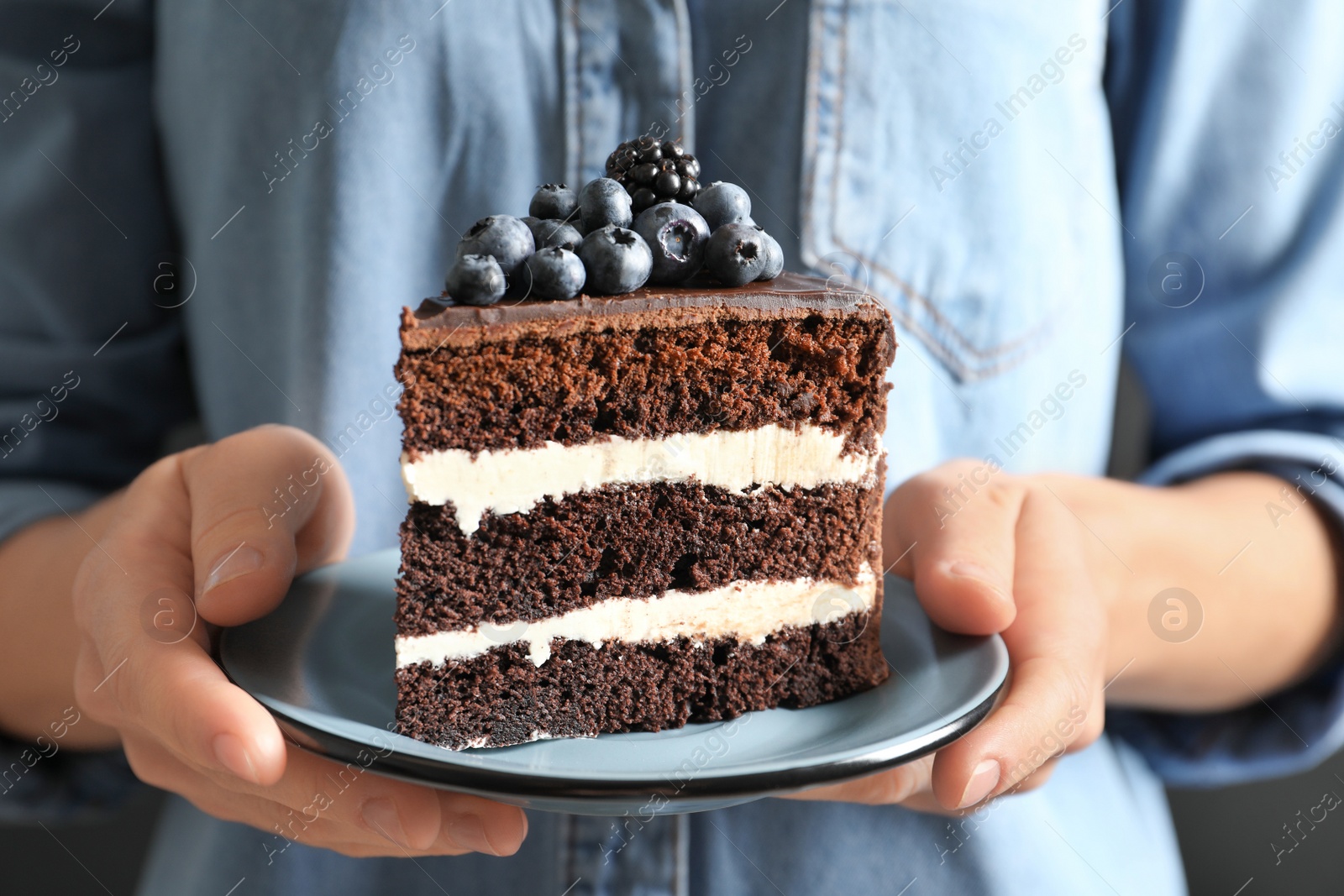 Photo of Woman holding plate with slice of chocolate sponge berry cake, closeup