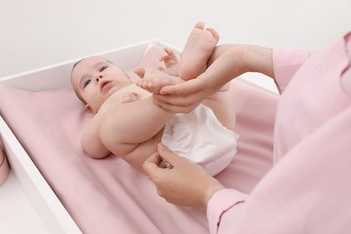 Mother changing baby's diaper at home, focus on hands