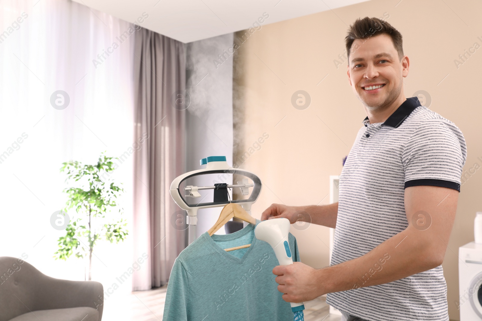 Photo of Man steaming his clothes on rack at home. Space for text