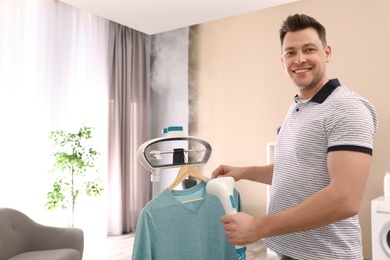 Photo of Man steaming his clothes on rack at home. Space for text