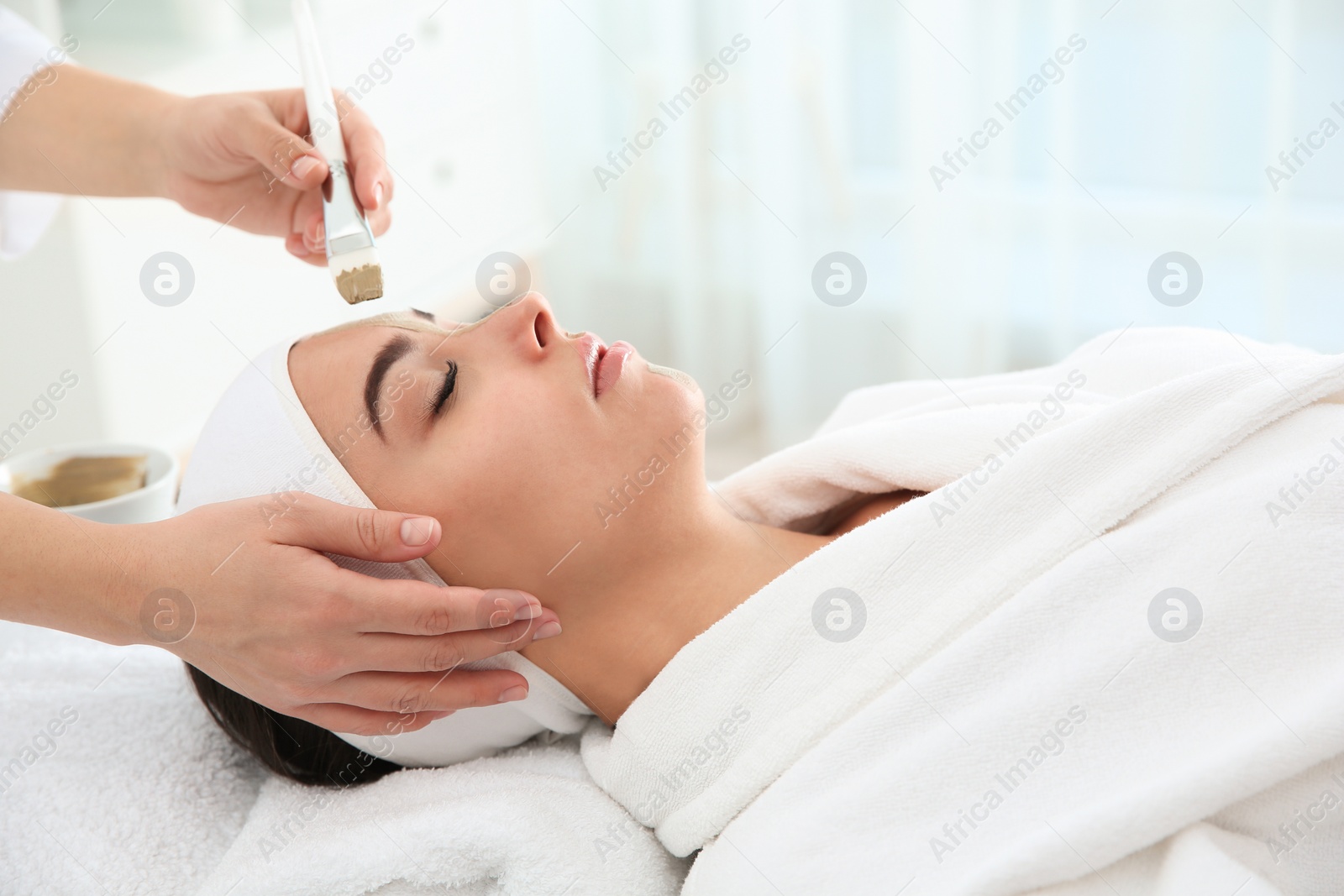 Photo of Cosmetologist applying mask on client's face in spa salon