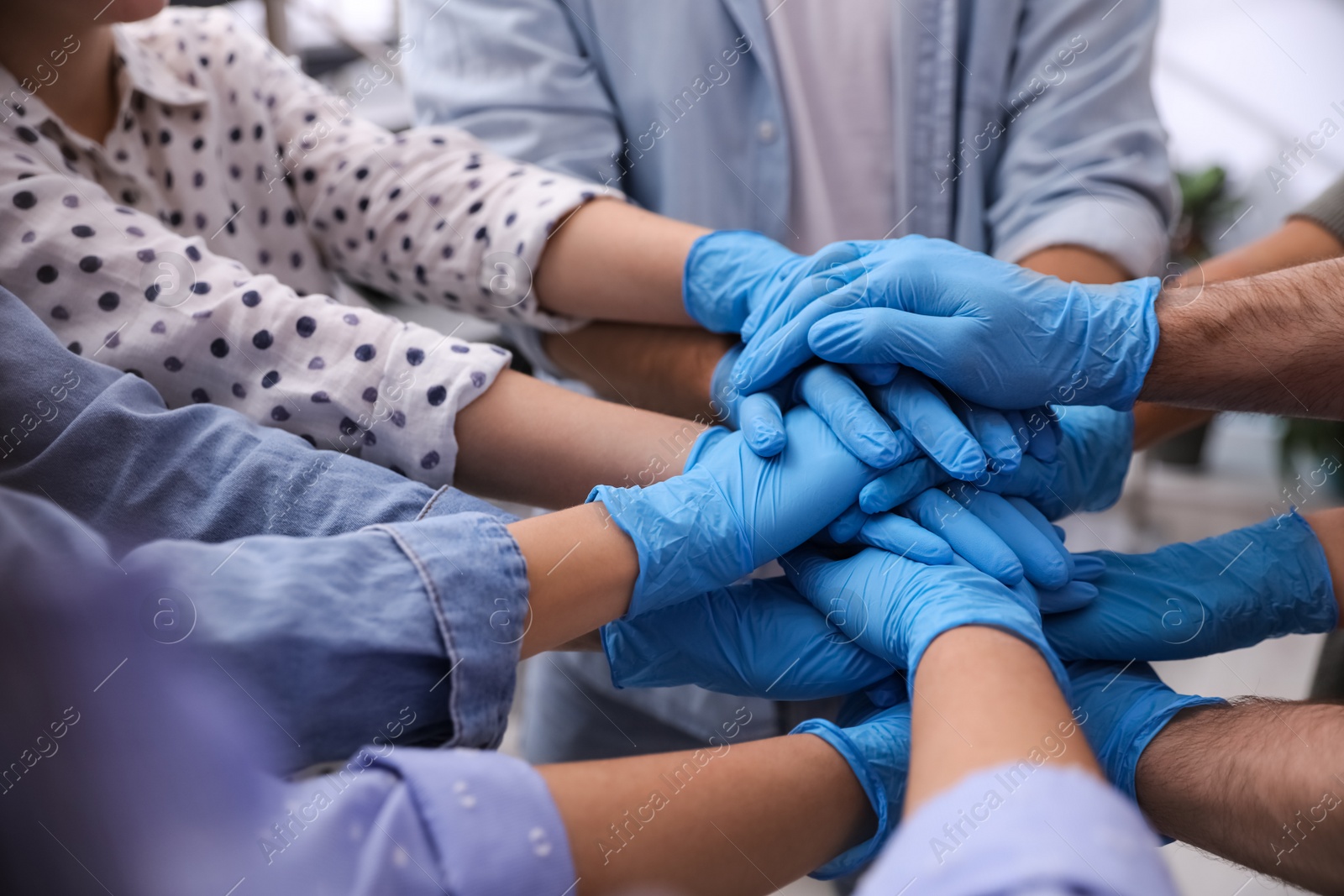 Photo of Group of people in blue medical gloves stacking hands indoors, closeup