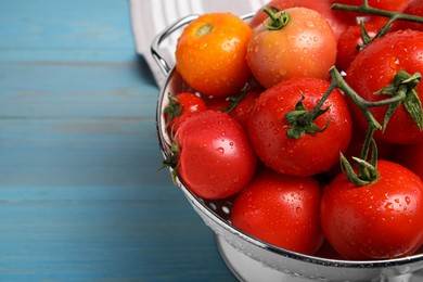 Photo of Many different ripe tomatoes in colander on light blue wooden table, closeup. Space for text