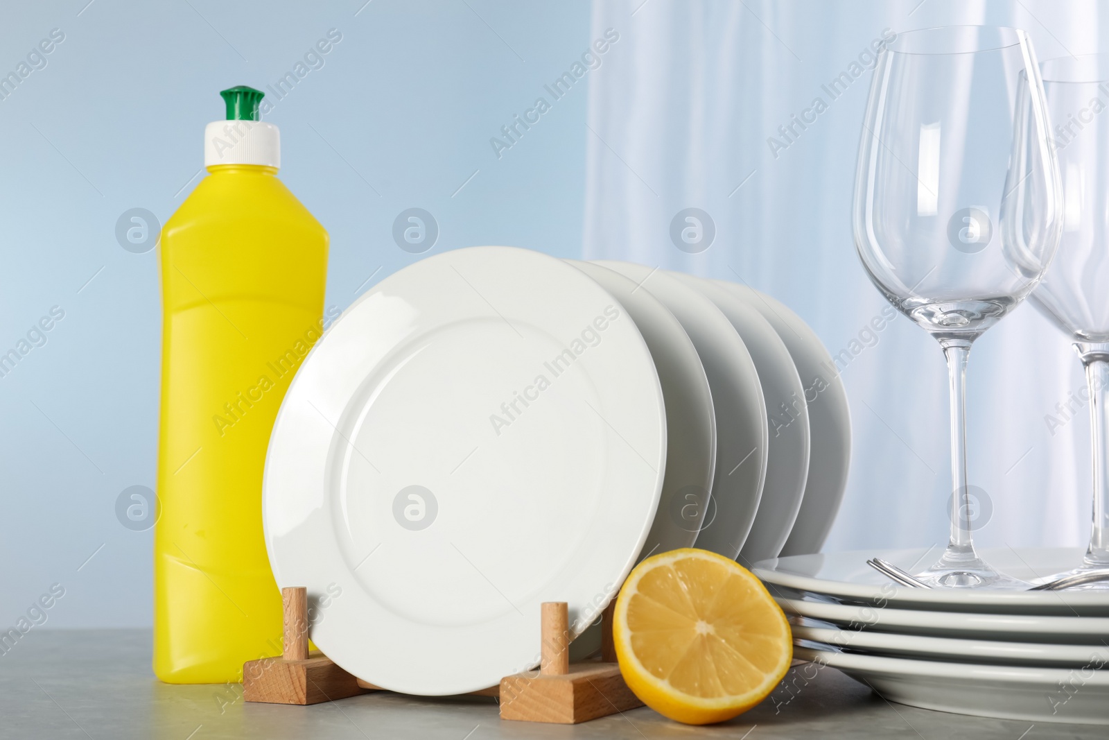 Photo of Glasses, clean dishware and bottle of detergent on grey marble table