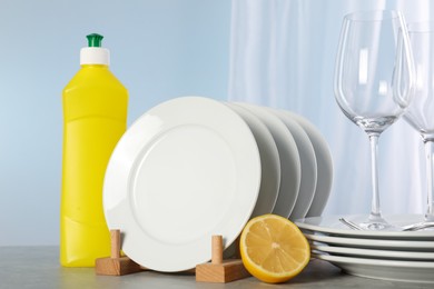 Glasses, clean dishware and bottle of detergent on grey marble table