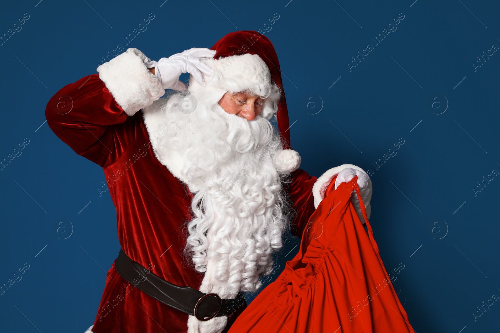 Photo of Authentic Santa Claus with bag full of gifts on blue background