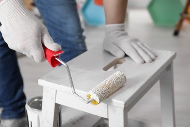 Photo of Man using roller to paint bekvam with white dye indoors, closeup