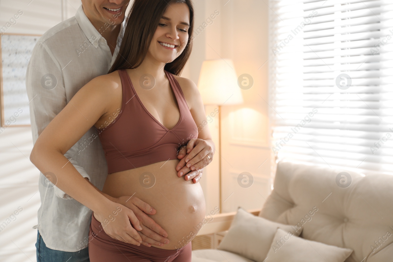 Photo of Man touching his pregnant wife's belly at home. Space for text