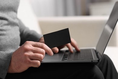 Man with laptop holding blank business card on blurred background, closeup