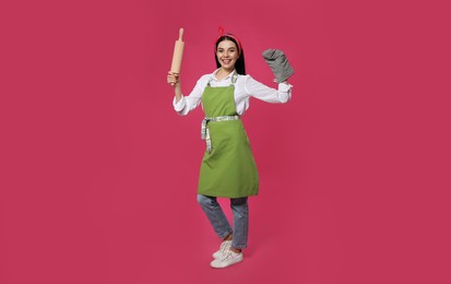 Photo of Young housewife in oven glove holding rolling pin on pink background