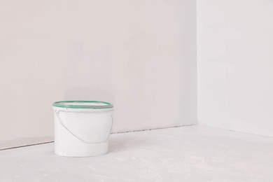 Photo of Bucket with paint in empty room, space for text