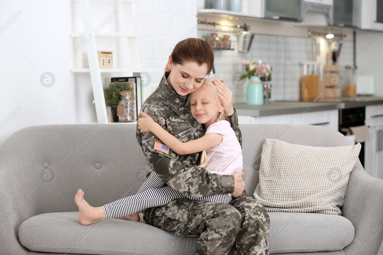 Photo of Woman in military uniform with her little daughter  on sofa at home