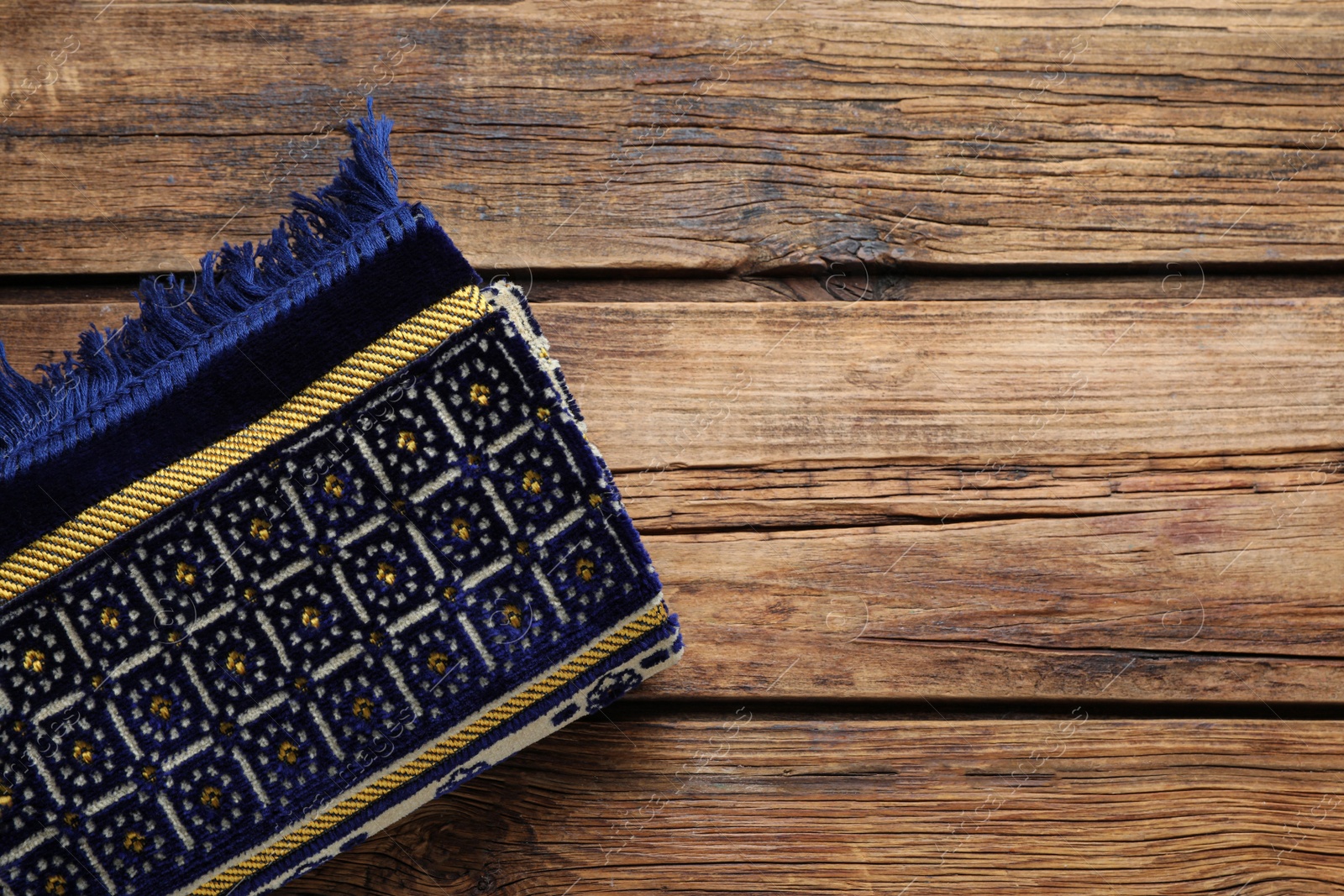 Photo of Muslim prayer rug on wooden table, top view. Space for text