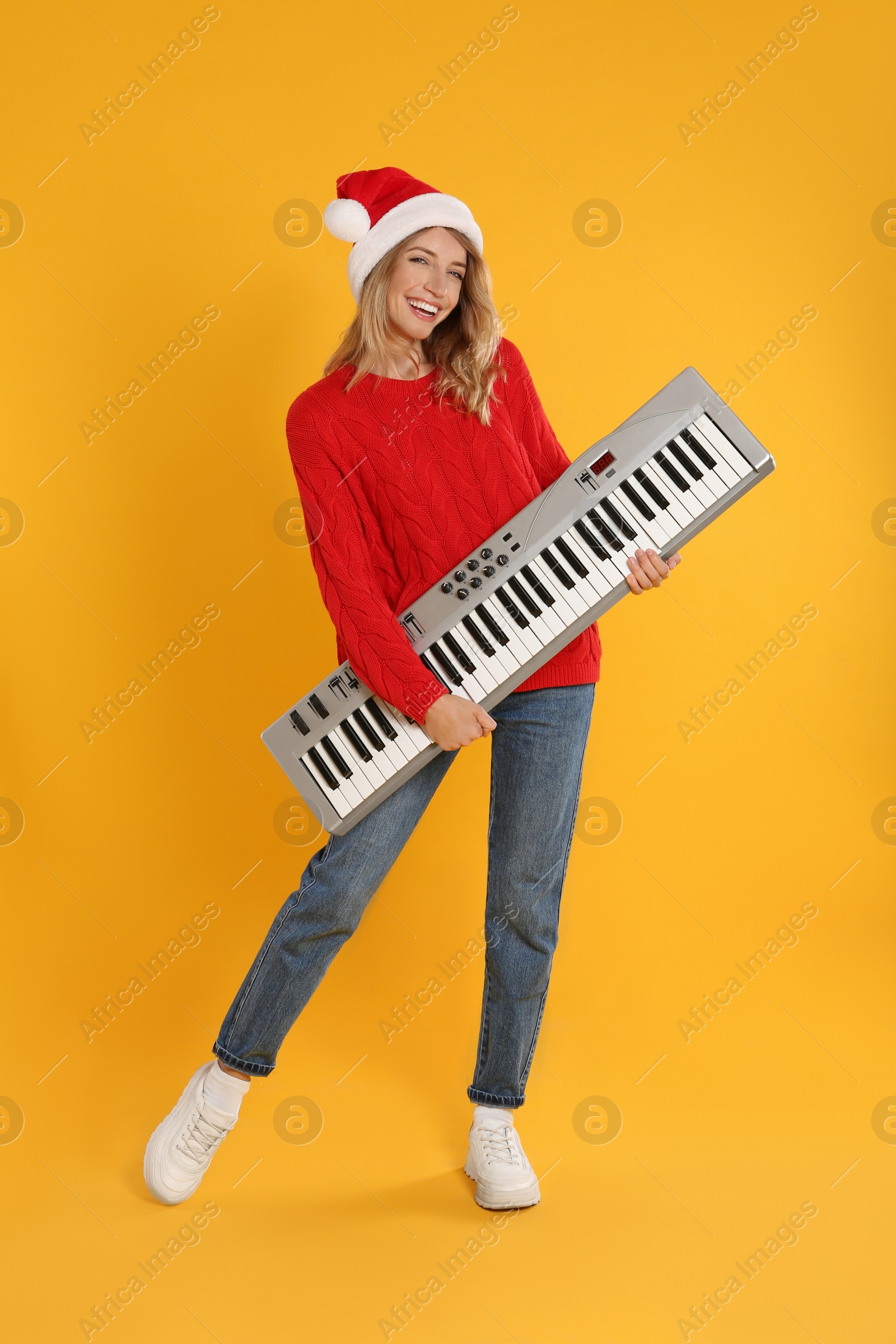 Photo of Young woman in Santa hat with synthesizer on yellow background. Christmas music