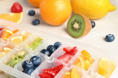 Ice cube tray with different fruits and berries on table, closeup