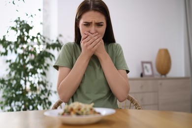 Photo of Young woman feeling nausea while seeing food at wooden table indoors