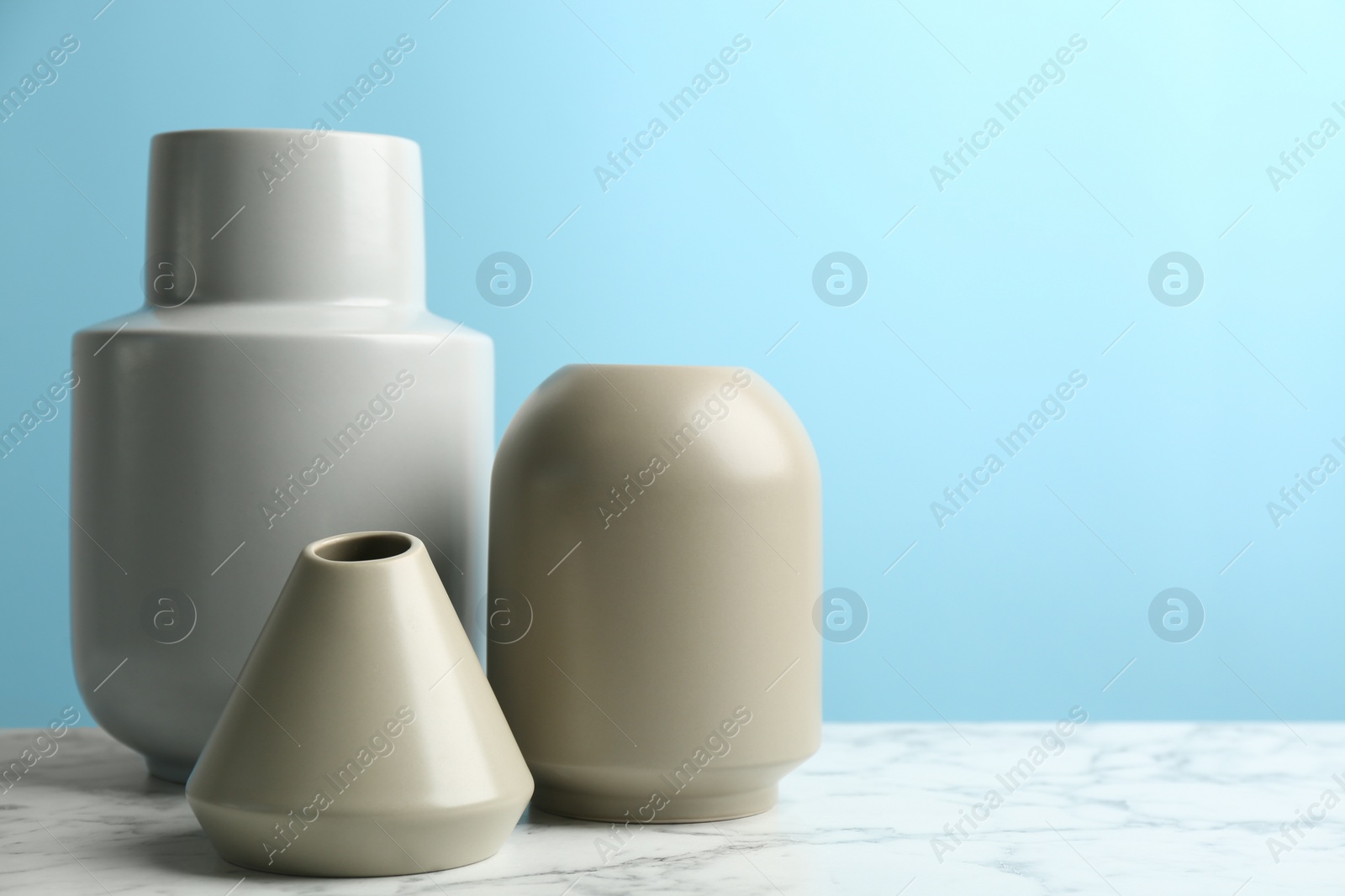 Photo of Stylish empty ceramic vases on white marble table against light blue background. Space for text