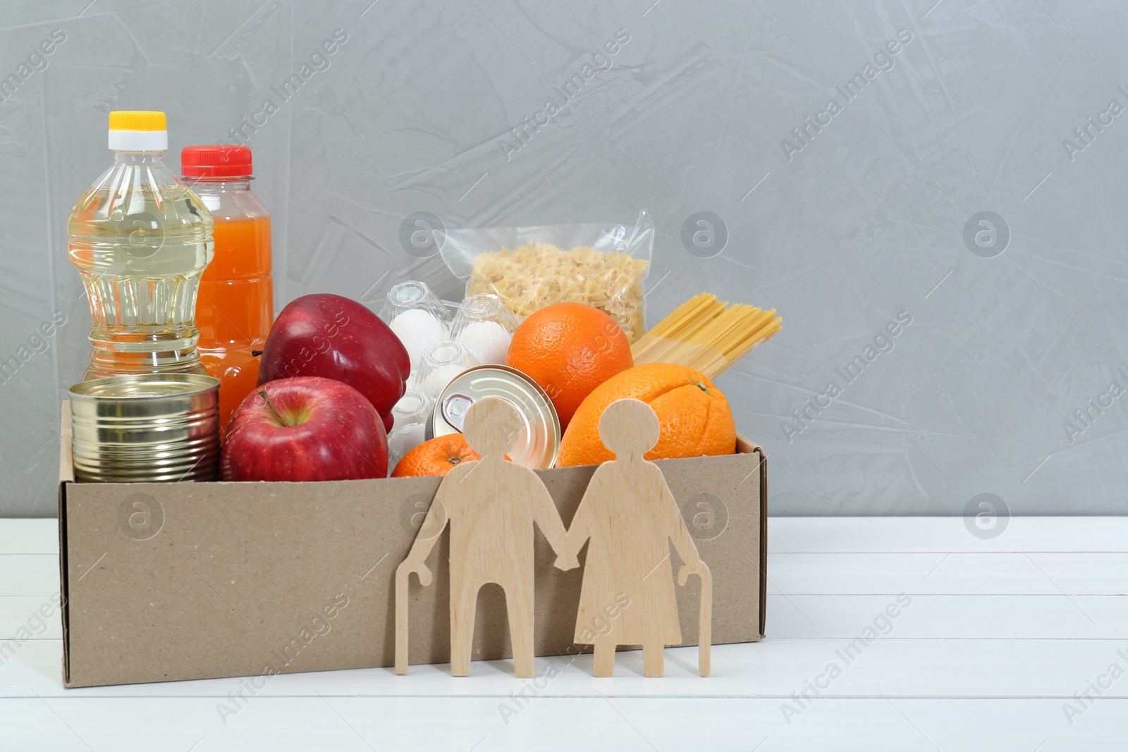 Photo of Humanitarian aid for elderly people. Different donation food products and figures of senior couple on white wooden table. Space for text