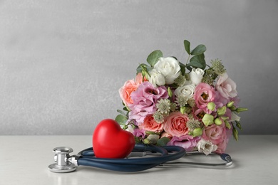 Photo of Red heart, stethoscope and bouquet on white table. World health day