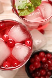 Tasty cranberry cocktail with ice cubes and mint in glasses on table, flat lay