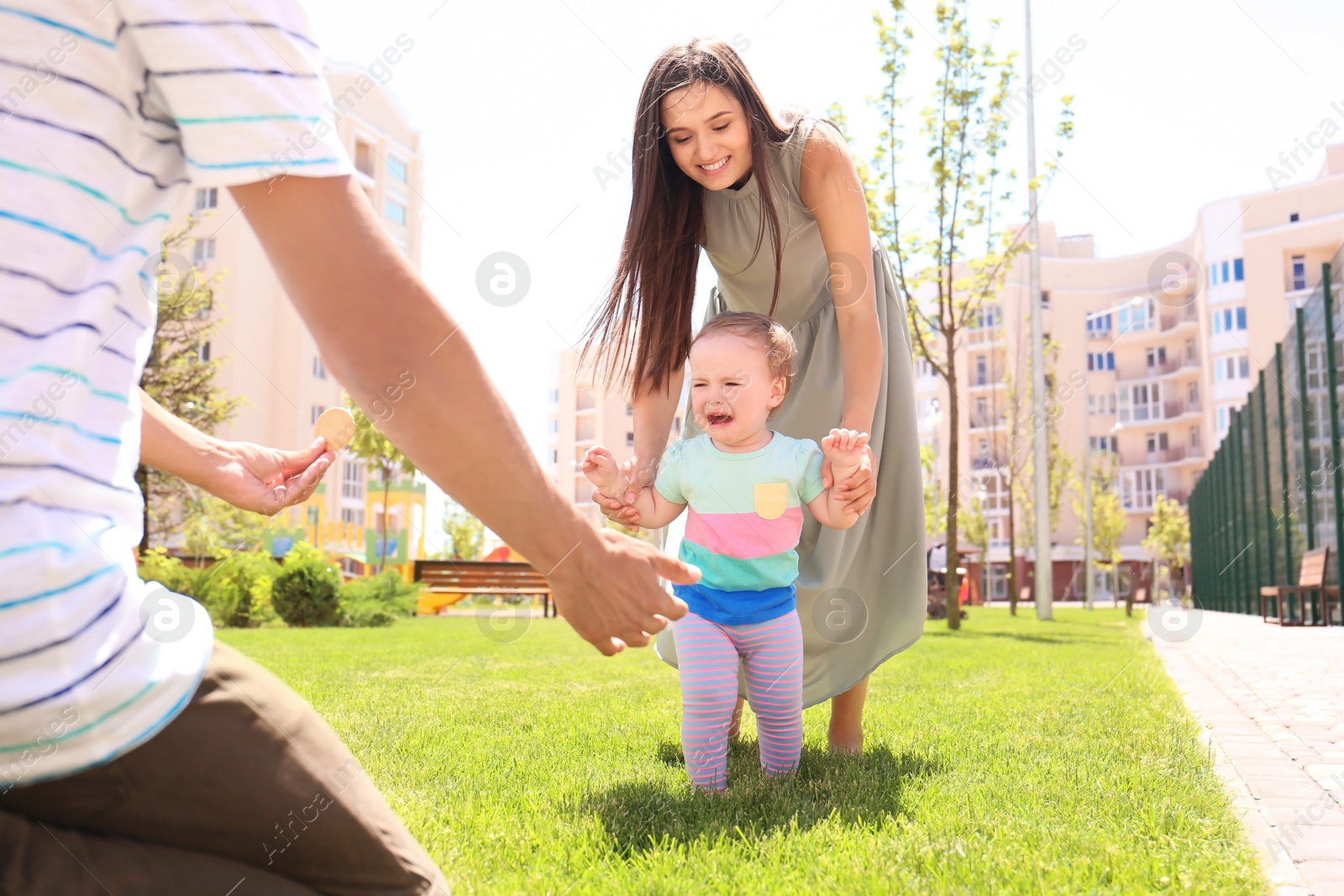 Photo of Parents supporting their baby daughter while she learning to walk outdoors