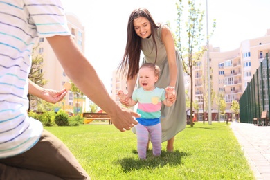 Parents supporting their baby daughter while she learning to walk outdoors