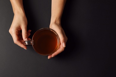 Woman with cup of tea on black background, top view. Space for text