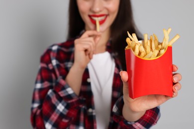 Beautiful young woman eating French fries on grey background, closeup