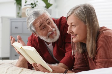 Lovely senior couple reading book on bed at home