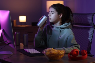Girl with energy drink playing computer game at table in room