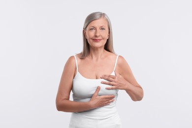 Beautiful senior woman doing breast self-examination on white background