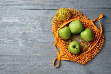 Photo of Net bag with fresh green apples on grey wooden table, top view. Space for text