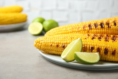 Photo of Plate of grilled corn cobs and lime slices on light grey table, closeup. Space for text