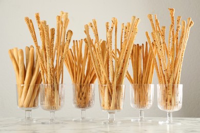 Delicious grissini sticks served in glasses on white marble table