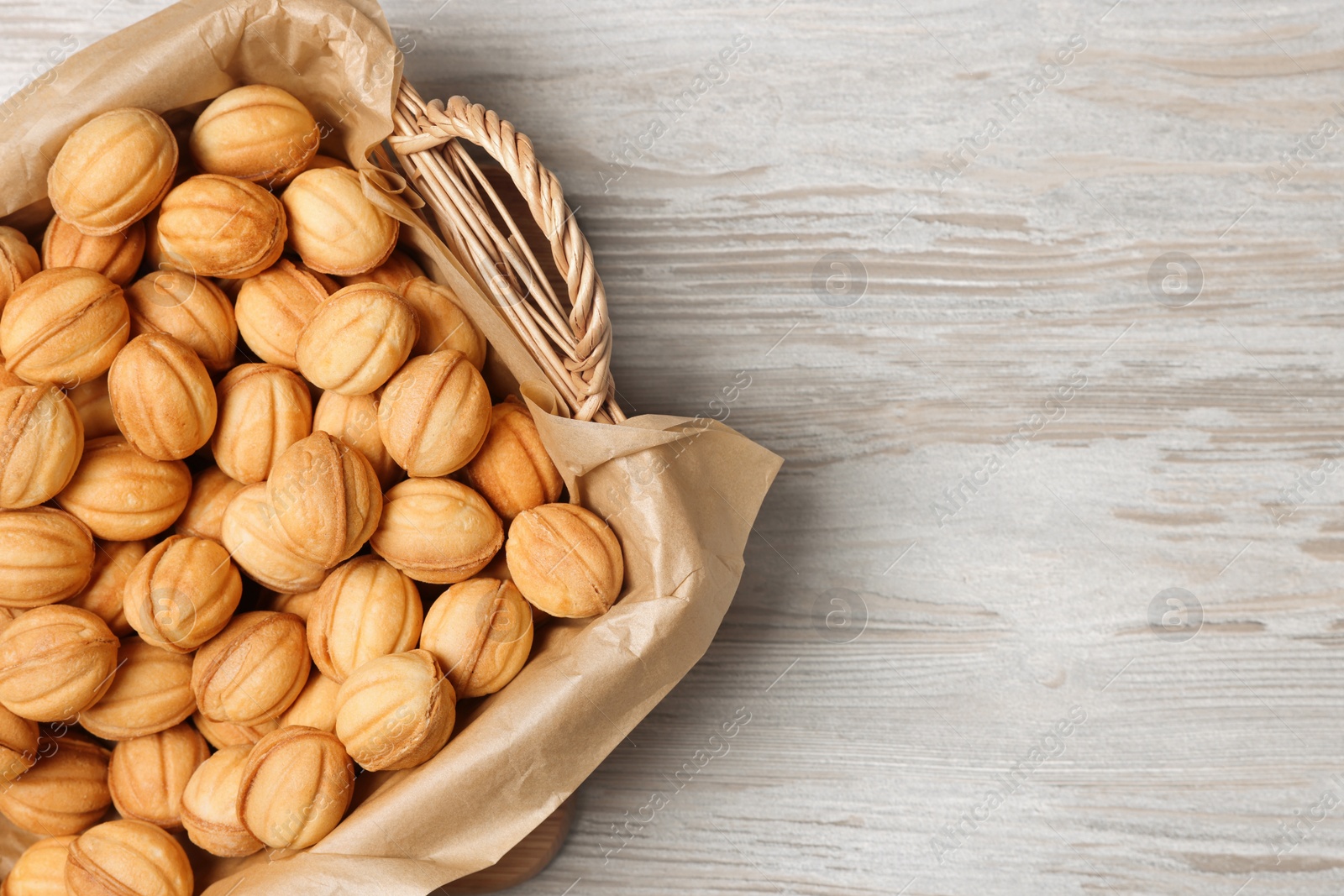 Photo of Wicker basket of delicious nut shaped cookies with boiled condensed milk on light wooden table, top view. Space for text