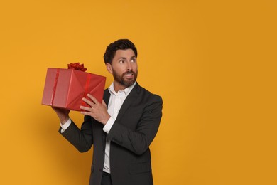 Photo of Emotional man holding gift box on yellow background, space for text