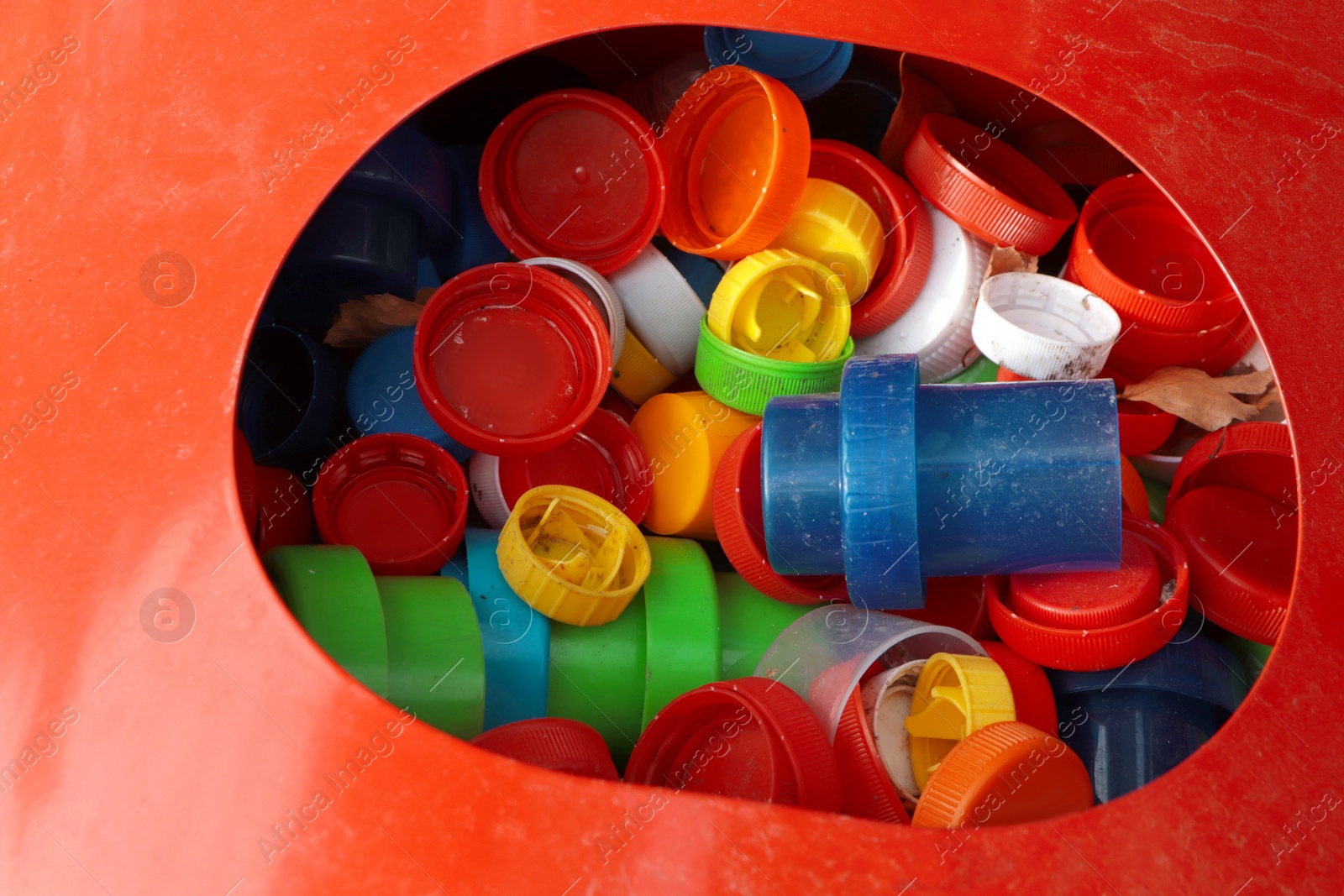 Photo of Different colorful bottle caps in red bin. Plastic recycling