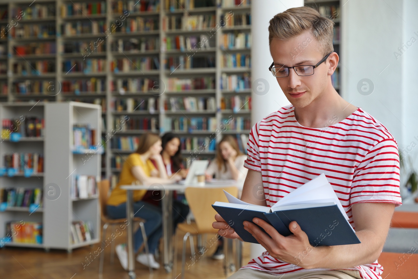 Photo of Young man reading book in library. Space for text