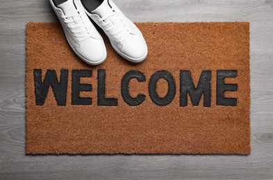 Photo of New clean mat with word WELCOME and shoes on floor, top view