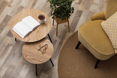 Photo of Wooden nesting tables near houseplant and armchair in room. Interior design