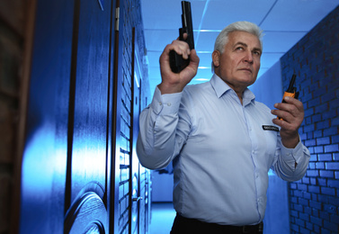 Photo of Professional security guard with gun and portable radio set in dark hallway