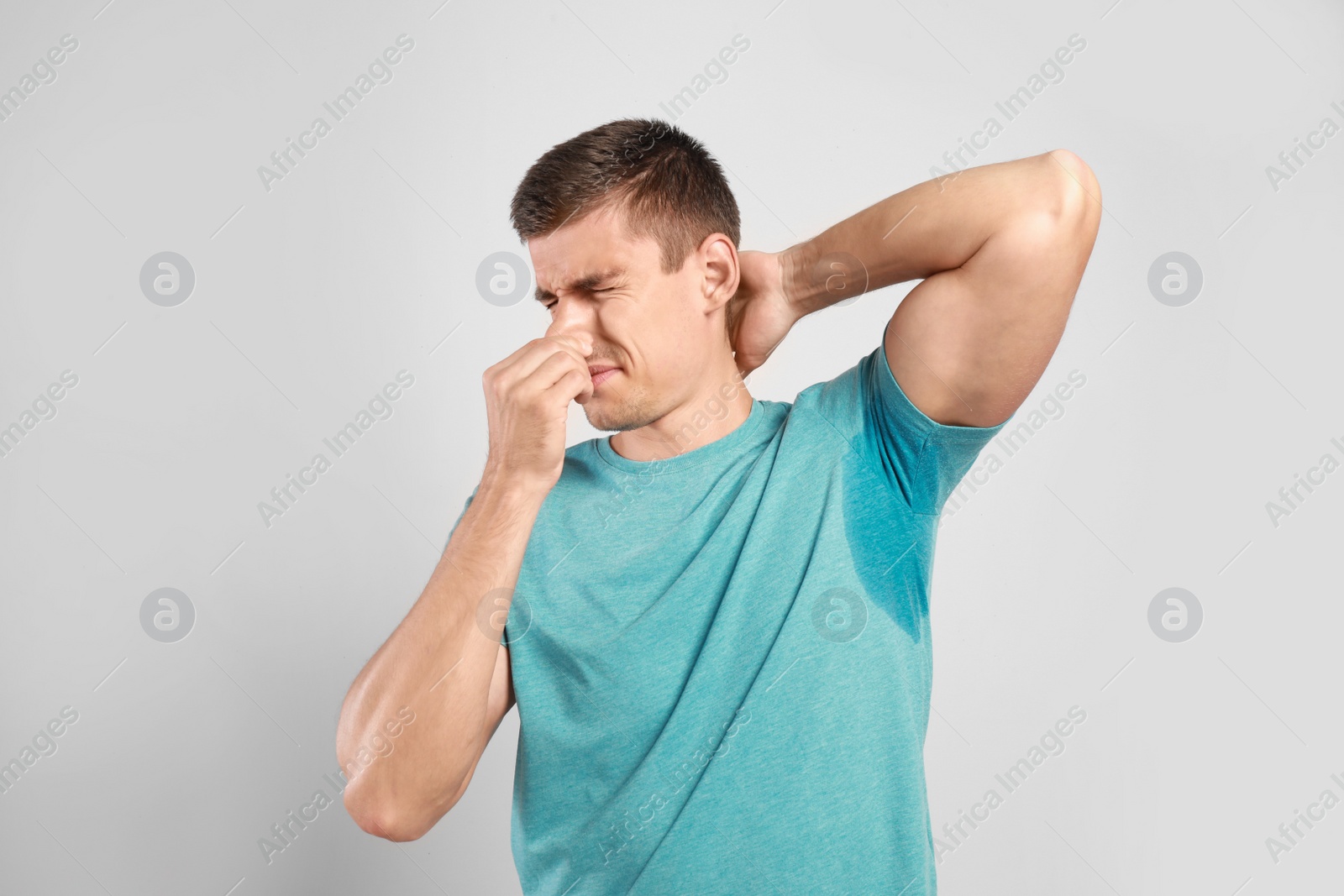 Photo of Young man with sweat stain on his clothes against light background. Using deodorant