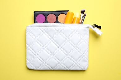 Photo of Bag with hygienic lipsticks and cosmetic products on yellow background, flat lay
