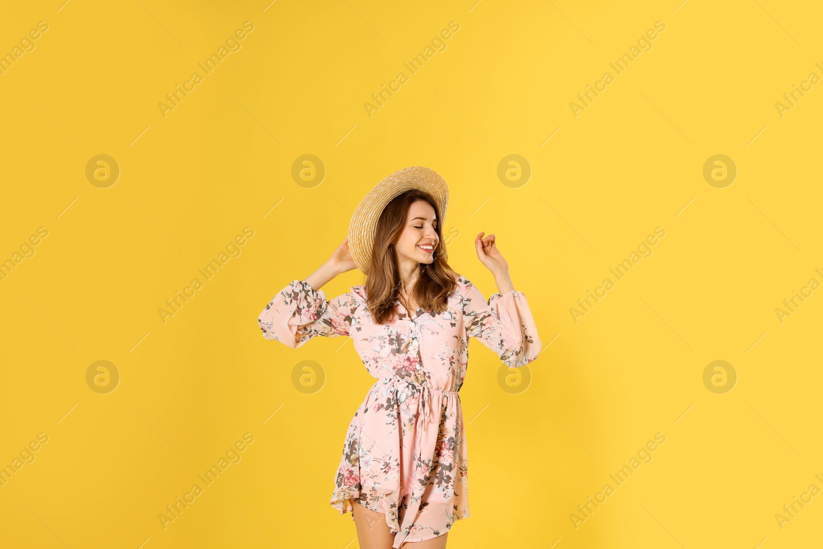 Photo of Young woman wearing floral print dress and straw hat on yellow background