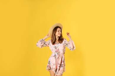 Photo of Young woman wearing floral print dress and straw hat on yellow background