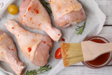 Photo of Marinade, brush, raw chicken drumsticks, rosemary and tomatoes on white wooden table, flat lay