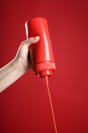 Photo of Woman pouring tasty ketchup from bottle on red background, closeup