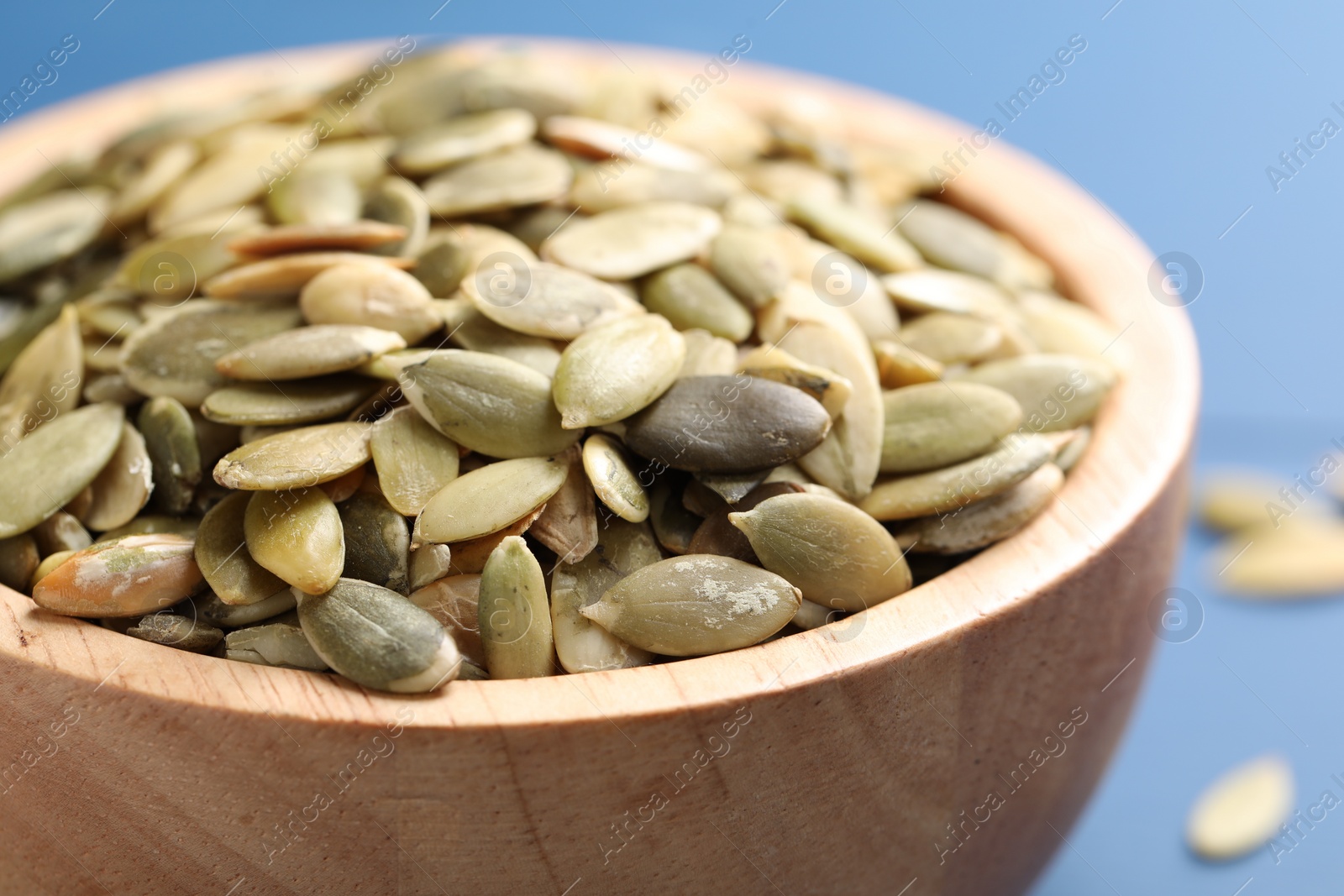 Photo of Wooden bowl with peeled pumpkin seeds on table, closeup