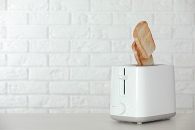 Photo of Bread slices popping up out of electric toaster on wooden table. Space for text